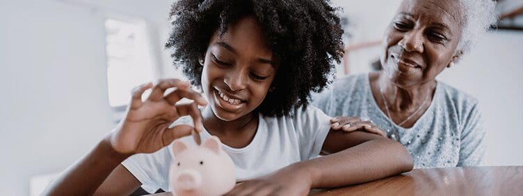 granddaughter-putting-coin-in-piggy-bank-smiling-with-her-grandmother