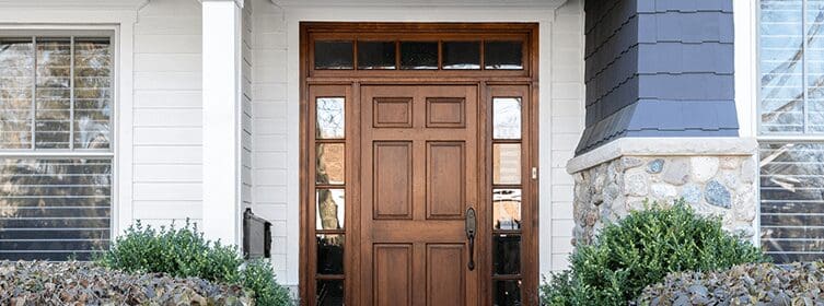 a-wooden-front-door-surrounded-by-windows-with-siding