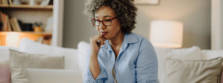 mature woman thinking on couch at home with laptop