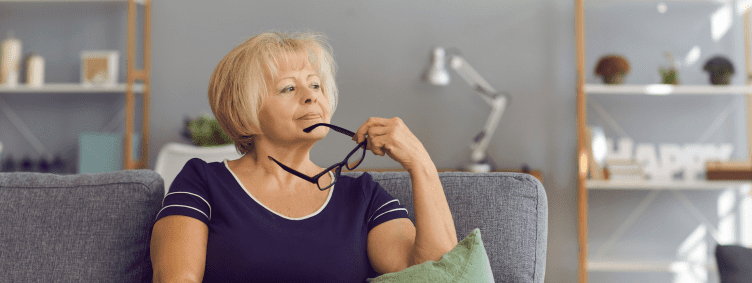 single mature woman thinking on couch at home with glasses