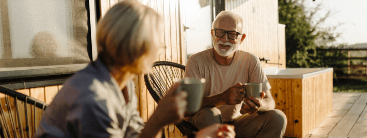 mature-senior-couple-sitting-outside-on-porch-talking-with-coffee